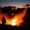 Fire personnel respond to homes destroyed while a helicopter drops water as the Palisades Fir