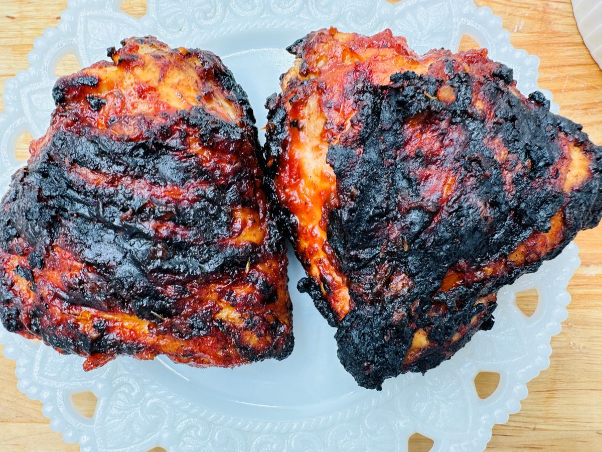 Two charred and glazed barbecue chicken thighs on a decorative white plate.