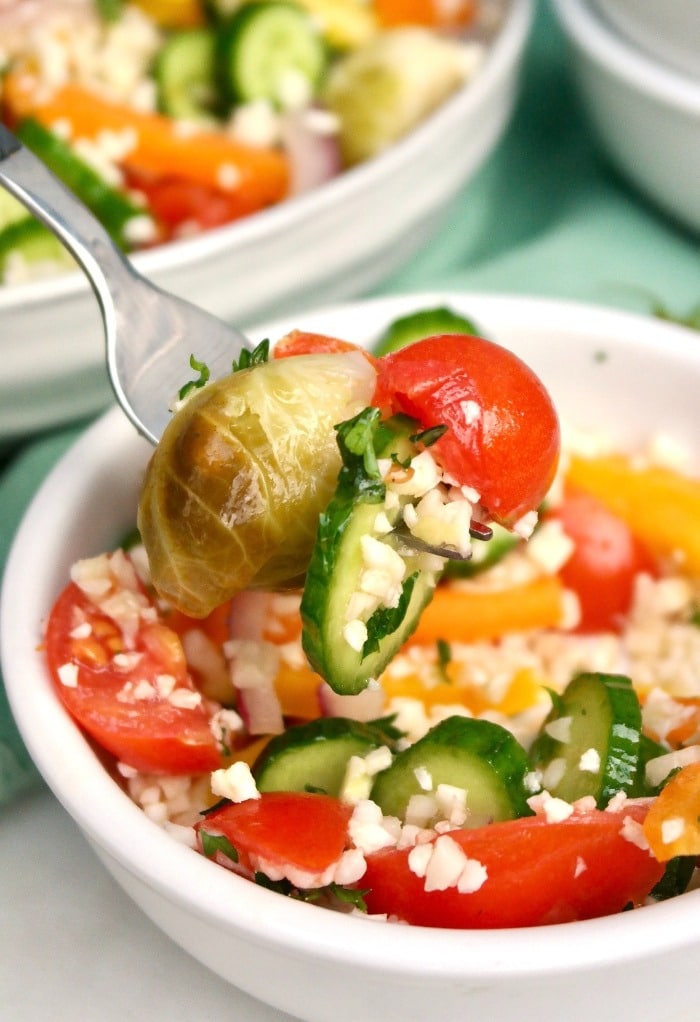 A forkful of cauliflower rice salad from a white bowl.