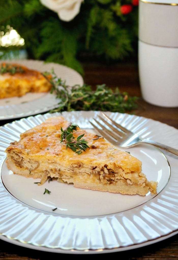 A slice of cheese and onion quiche topped with fresh thyme on a white and gray plate.