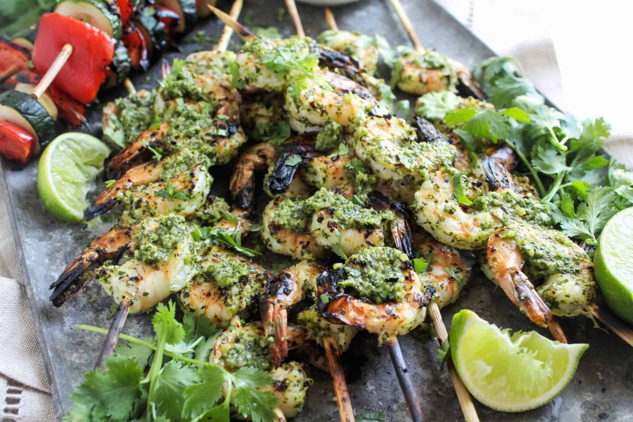 Grilled shrimp skewers topped with chimichurri sauce, served with fresh herbs and lime.