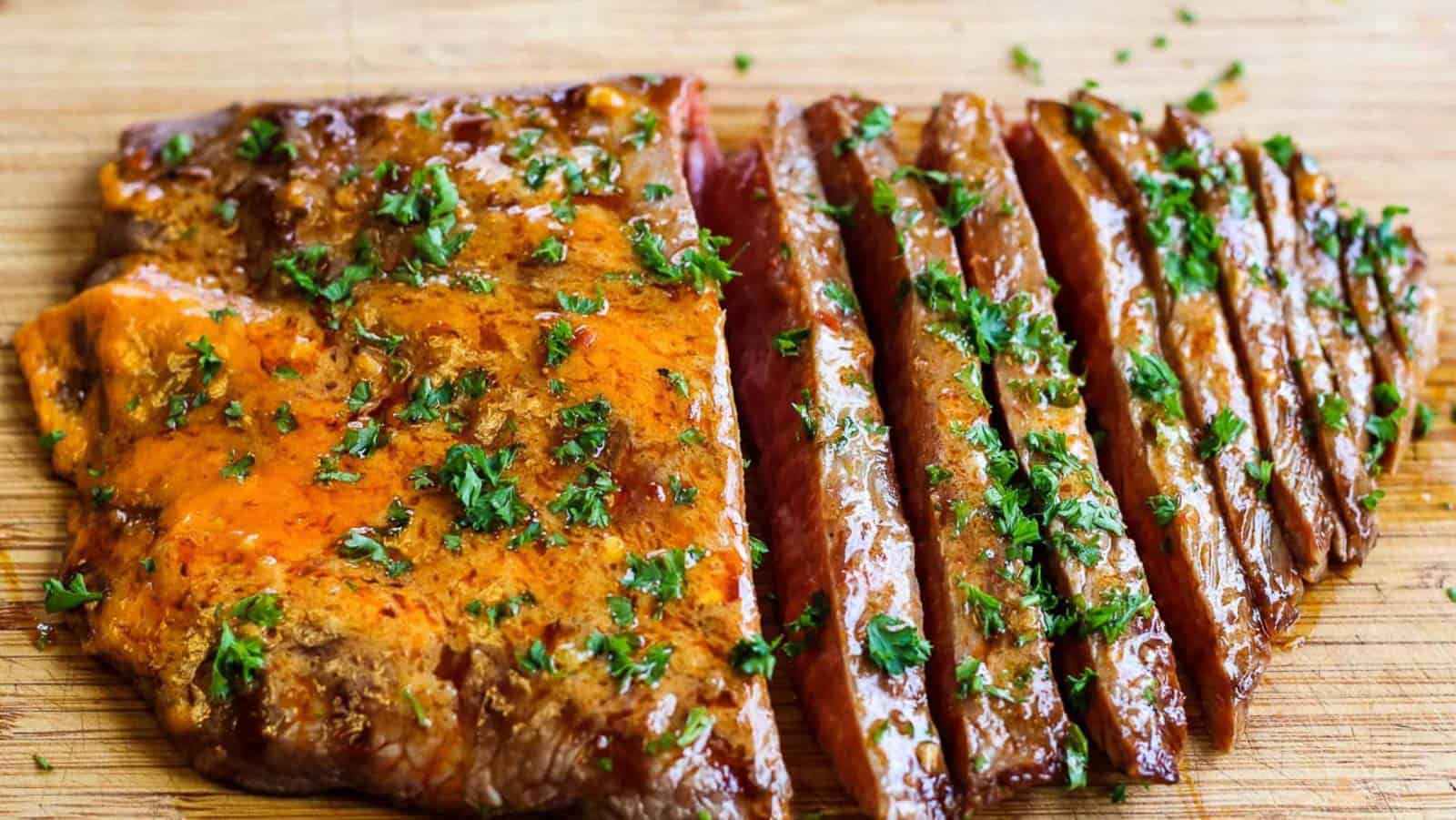 Sliced grilled flank steak topped with herbs on a wooden cutting board.
