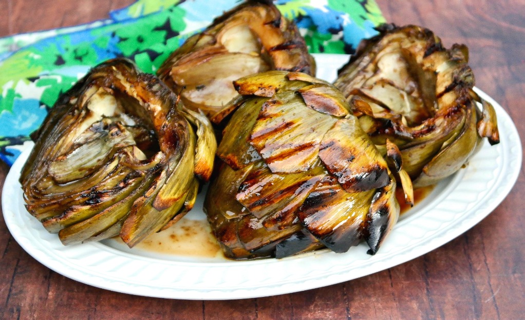 Horizontal view of cooked artichokes on a white serving platter.
