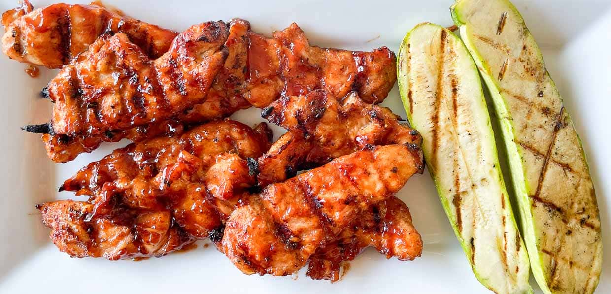 Barbecue grilled chicken tenders and grilled zucchini slices on a white plate.
