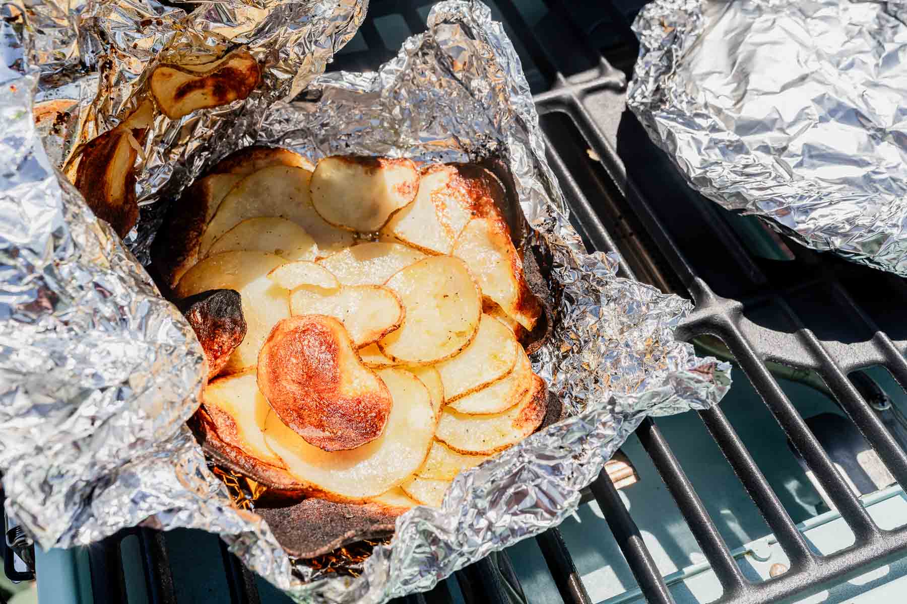 Sliced potatoes with crispy edges in a foil packet on a grill.