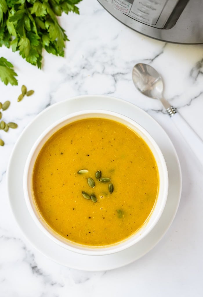 A white bowl filled with butternut squash soup topped with pumpkin seeds.