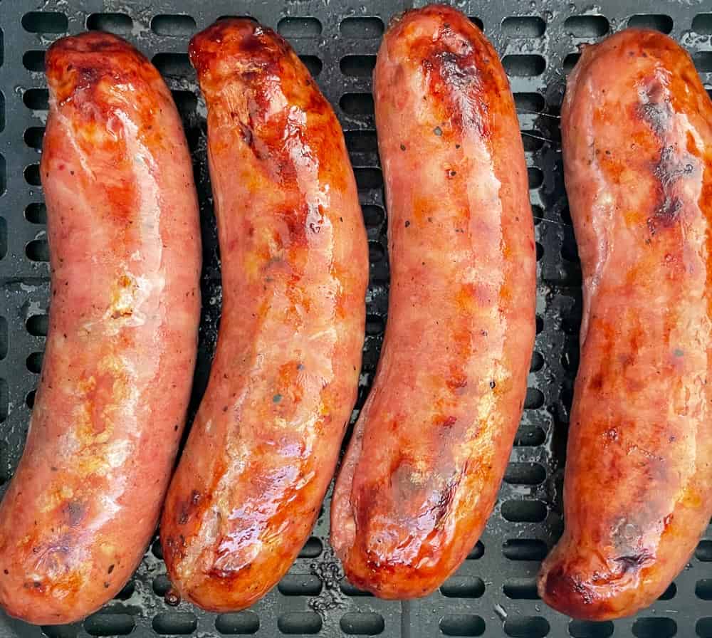 Four grilled sausages lined up on a dark grill pan.