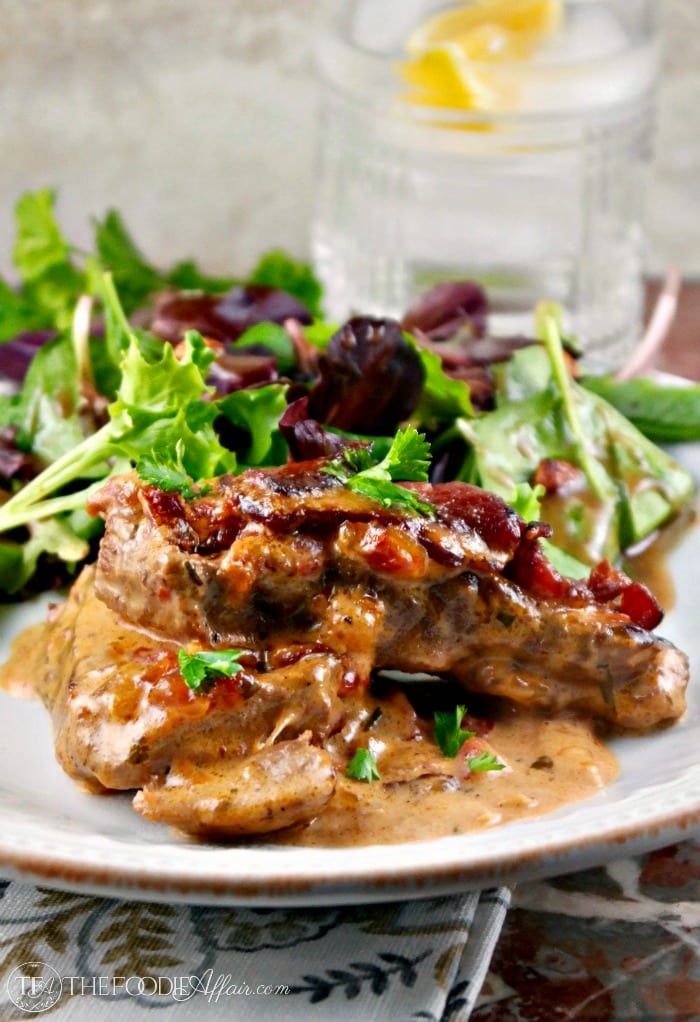 skillet pork chops topped with caramelized onions and bacon on a white plate
