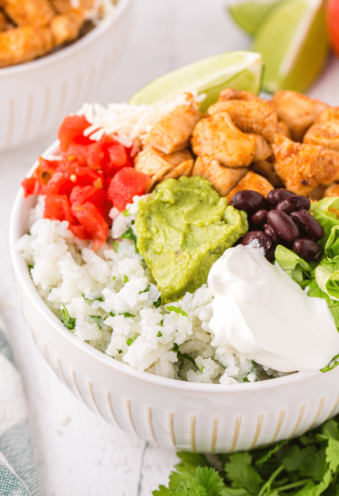 A white bowl with chicken and all the ingredients in a burrito.