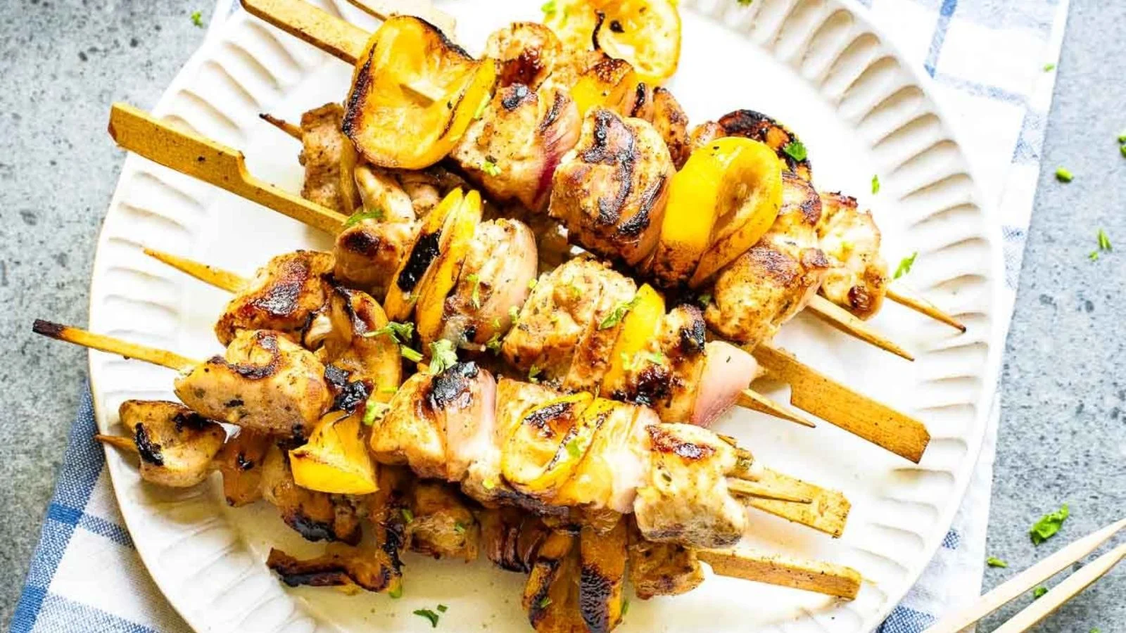 Grilled chicken kabobs with yellow bell peppers and onions on a white plate.